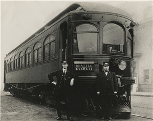 Two men in conductor uniforms stand at the front of a shiny black train car that says Seattle Everett on the front